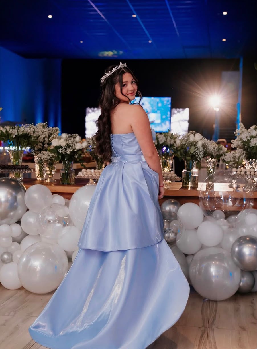 Debutante de vestido azul claro com coroa em meio à decoração da festa