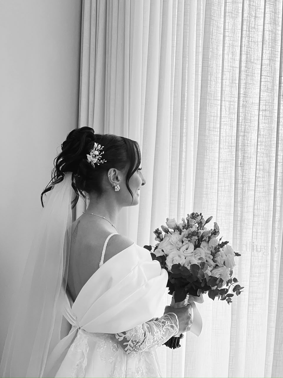 Noiva em retrato preto e branco, de perfil com véu e buquê